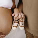 Expectant couple holding tiny brown baby shoes, symbolizing upcoming parenthood.