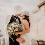 Bride and groom share a tender kiss under a veil, showcasing love and romance on their special day.