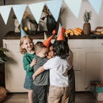 Group of kids hugging and smiling at a birthday party indoors with decorations.