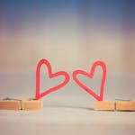 Two wooden clothespins with red heart shapes, symbolizing love and romance, on a blurred background.