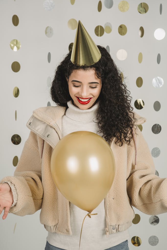 A happy woman in winter clothing celebrating indoors with a gold balloon.